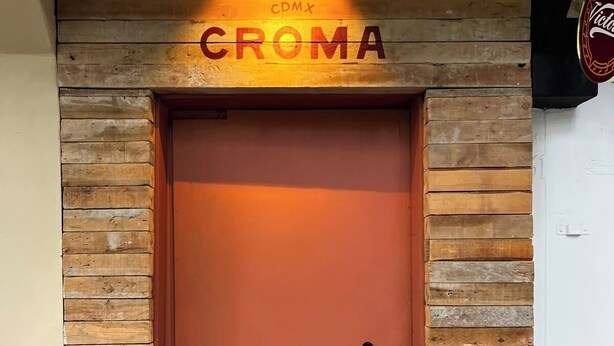 Een houten deur met een rode omlijsting en een bord erboven met de tekst 'CROMA'.