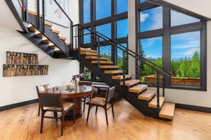 Un interior moderno con una escalera, piso de madera y ventanas amplias que ofrecen vistas a la vegetación.