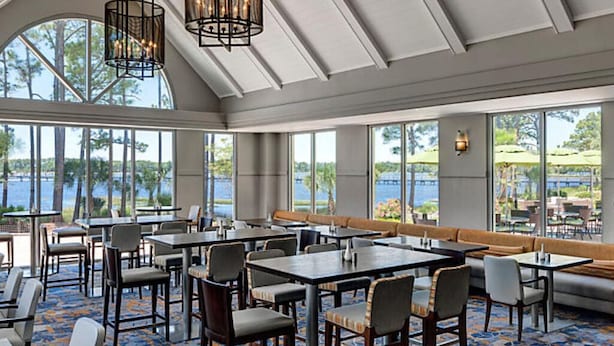 A restaurant with tables and chairs, large windows, and a view of the outdoors.