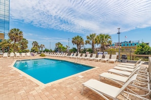 A swimming pool with lounge chairs, palm trees, and a building in the background.