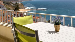 Un balcón con mesa y silla, con vista al mar y una playa.