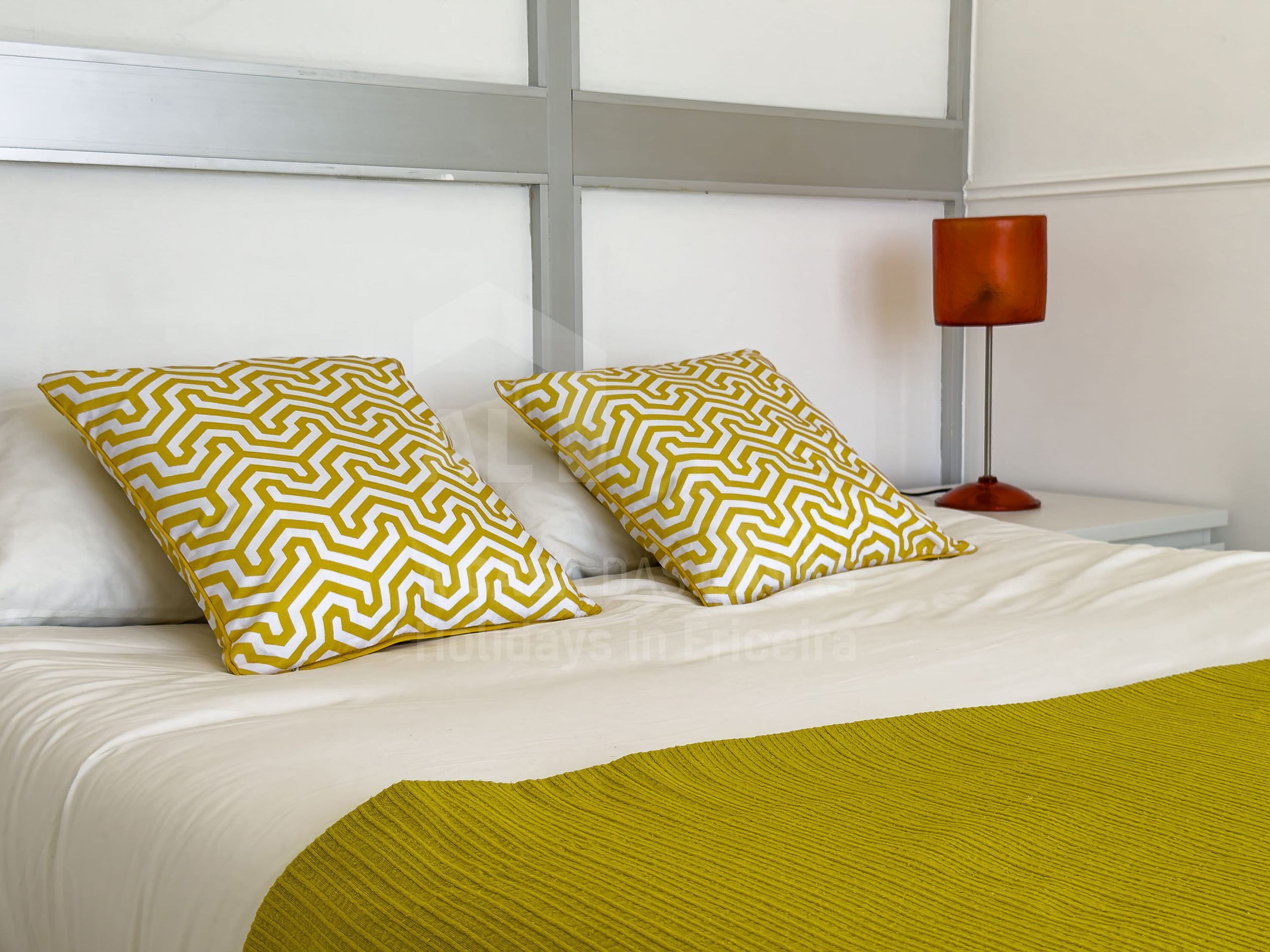 A bed with two patterned pillows, a bedside lamp, and a green throw blanket.
