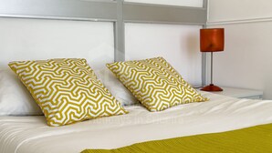 Una cama con dos almohadones estampados, una lámpara de noche y un plaid verde.