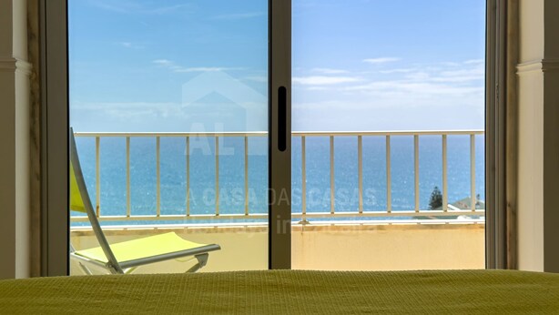 Una habitación con cama, un balcón con una silla y vista al mar.