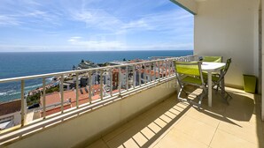 Un balcón con vistas al mar y edificios, una mesa con sillas y una planta en maceta.