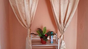 Une pièce avec des rideaux de couleur beige, une étagère sur laquelle est posée une plante en pot et deux bouteilles.