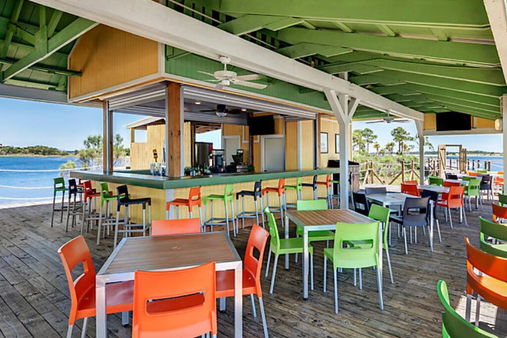 Een buitenterras met houten tafels en stoelen, een bar en uitzicht op zee.