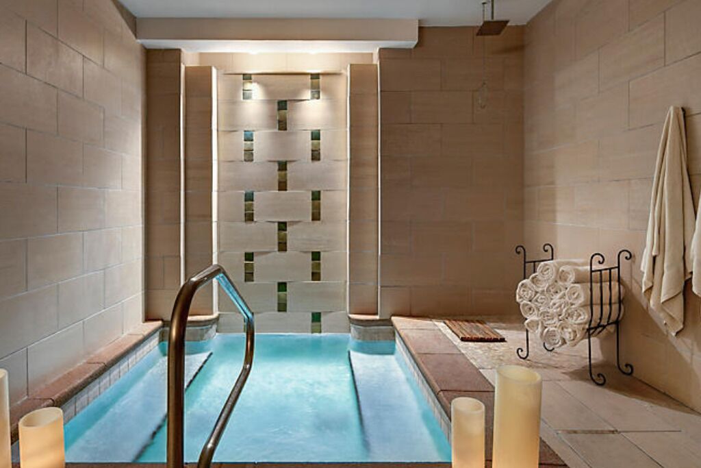 Een wellnessruimte met een jacuzzi, een muur met een geometrisch patroon, en een handdoekrek met opgevouwen handdoeken.