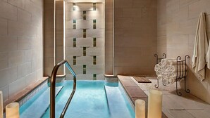 A spa area with a hot tub, a wall with a geometric pattern, and a towel rack with folded towels. - Bayside 1br BLOCK (Panama City Beach)