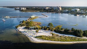 An aerial view of a coastal area with a beach, a pier, and buildings in the background. - Bayside 1br BLOCK (Panama City Beach)