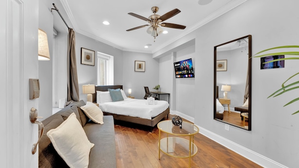 A hotel room with a bed, a sofa, a small table, a ceiling fan, a TV, and a mirror. - Apartmint at 1149 N 3rd St Philladelphia (Philadelphia)