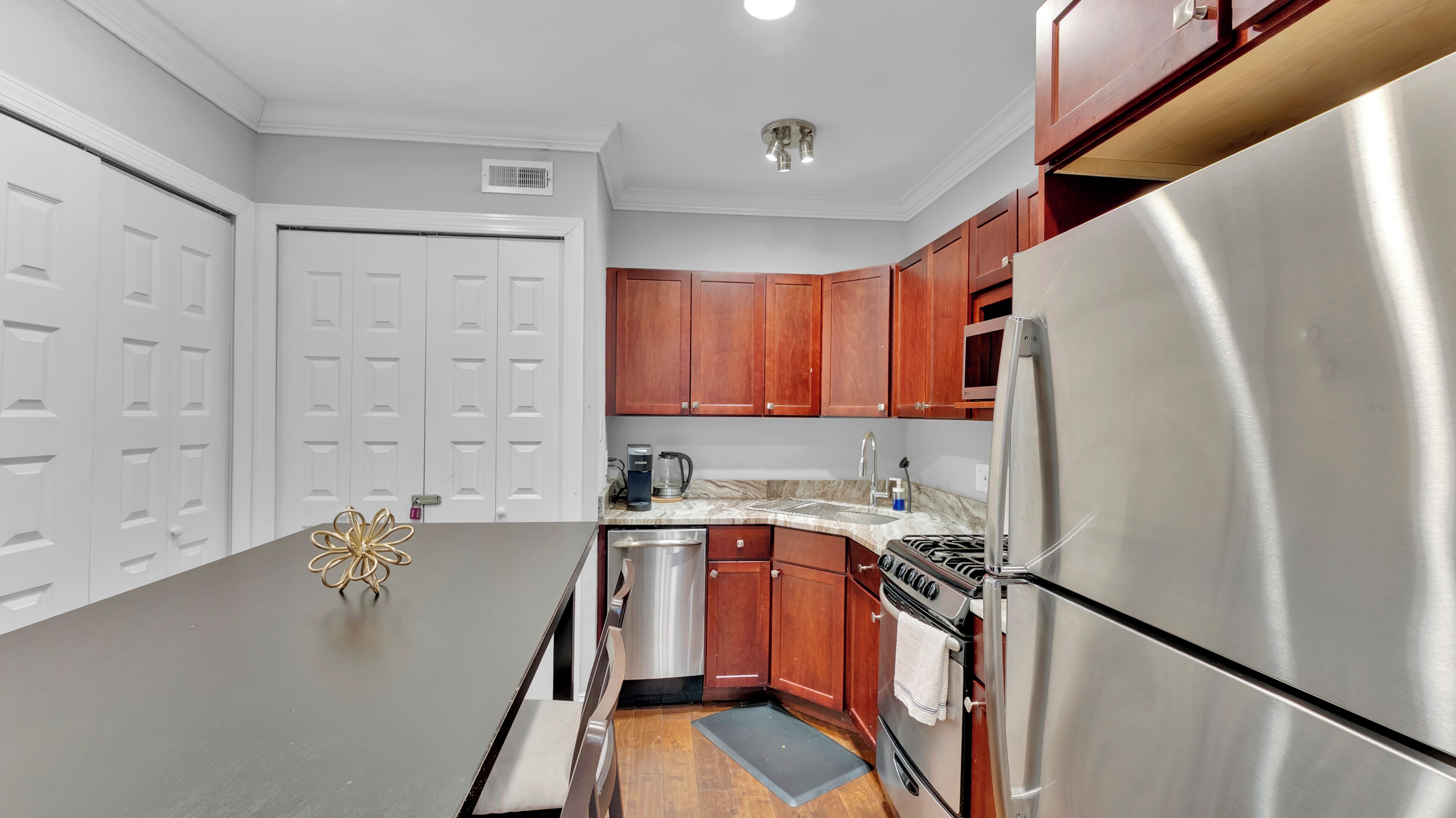 A kitchen with white cabinets, a stainless steel refrigerator, a stove, and a coffee maker.