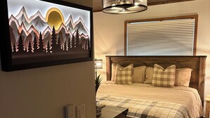 A bedroom with a bed, a mounted TV, a ceiling fan, and a window with blinds.