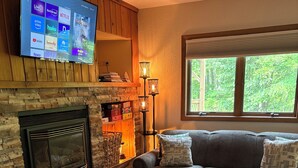 A living room with a stone fireplace, a sofa, a coffee table, and a TV mounted on the wall.