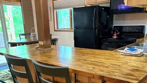 A kitchen with wooden cabinets, a black refrigerator, a stove, and a dining area with chairs and a table.