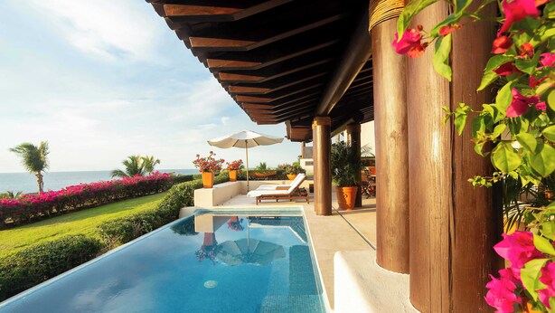 A swimming pool with lounge chairs and umbrellas, surrounded by greenery and a view of the sea. - Four Seasons Villa Riva | 4BR Ocean-View Retreat w/ Infinity Pool & Golf Cart (Punta Mita)