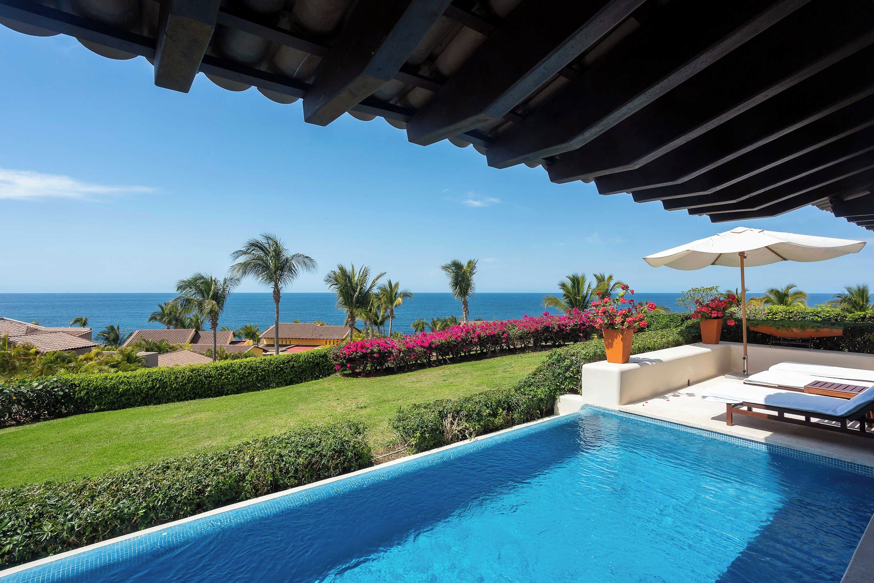 Ein Poolbereich mit Blick auf das Meer, umgeben von Palmen und einem klaren Himmel.