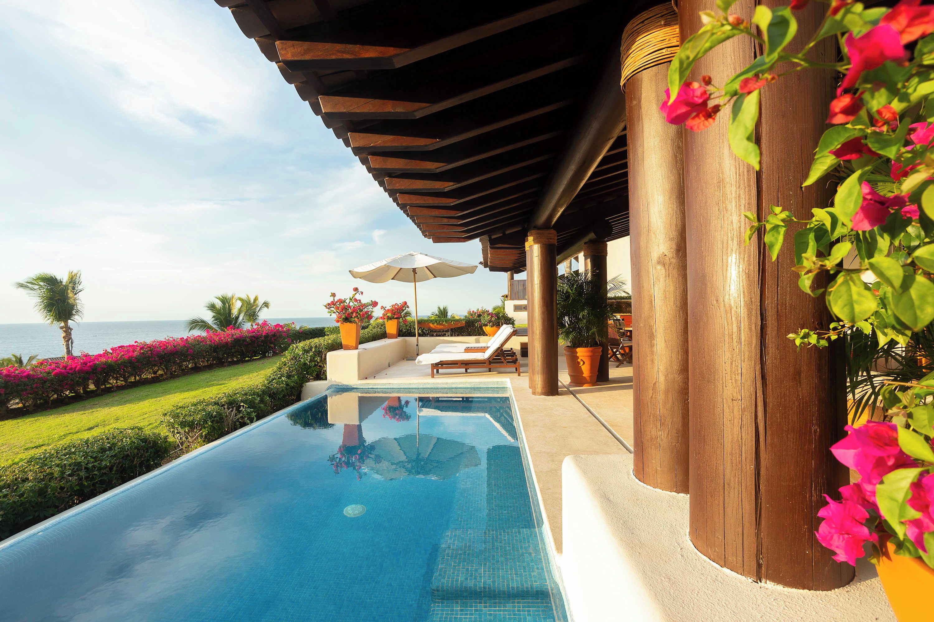 A poolside area with a clear view of the ocean, a lounge chair, and potted plants.