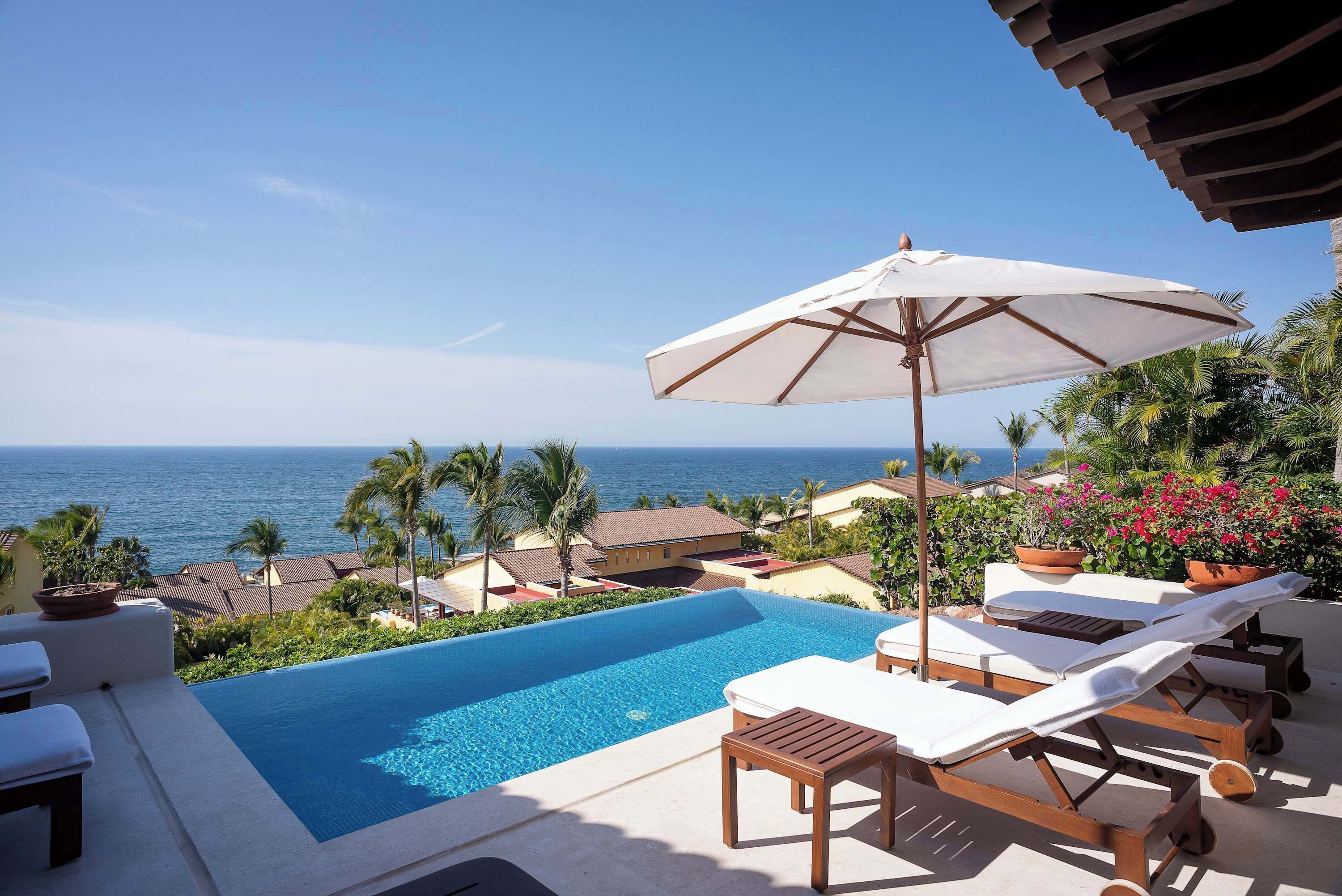 Une piscine à débordement avec des chaises longues et un parasol, offrant une vue sur l’océan.