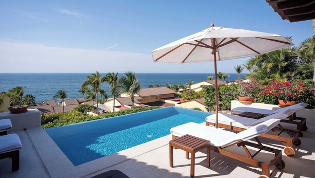 Uma piscina infinita com espreguiçadeiras e um guarda-sol, com vista para o oceano.