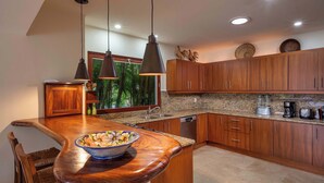 A kitchen with wooden cabinets, a granite countertop, a bowl on the counter, and pendant lighting. - Luxury Golf-Front Villa: 6BR w/ Private Pool, Chef & Golf Cart (Punta Mita)