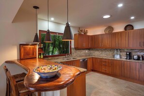 A kitchen with wooden cabinets, a granite countertop, a bowl on the counter, and pendant lighting. - Luxury Golf-Front Villa: 6BR w/ Private Pool, Chef & Golf Cart (Punta Mita)