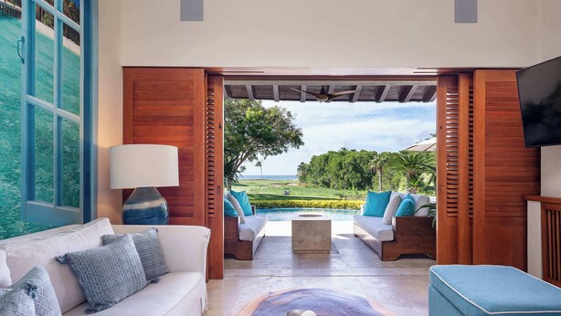 A modern living room with a view of a pool and greenery, a wooden ceiling, and a flat-screen TV. - Luxury Golf-Front Villa: 6BR w/ Private Pool, Chef & Golf Cart (Punta Mita)