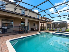 Ein überdachter Pool im Freien mit einer Terrasse, einem Grill und Liegestühlen.