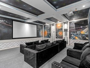 Ein Heimkino mit einer großen Leinwand, Liegesesseln und Wandbildern zum Thema Weltraum.