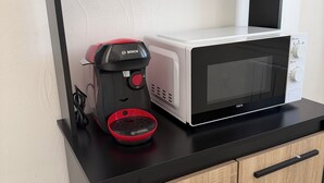 Una cocina equipada con microondas, cafetera y una repisa con tazas y hervidor.