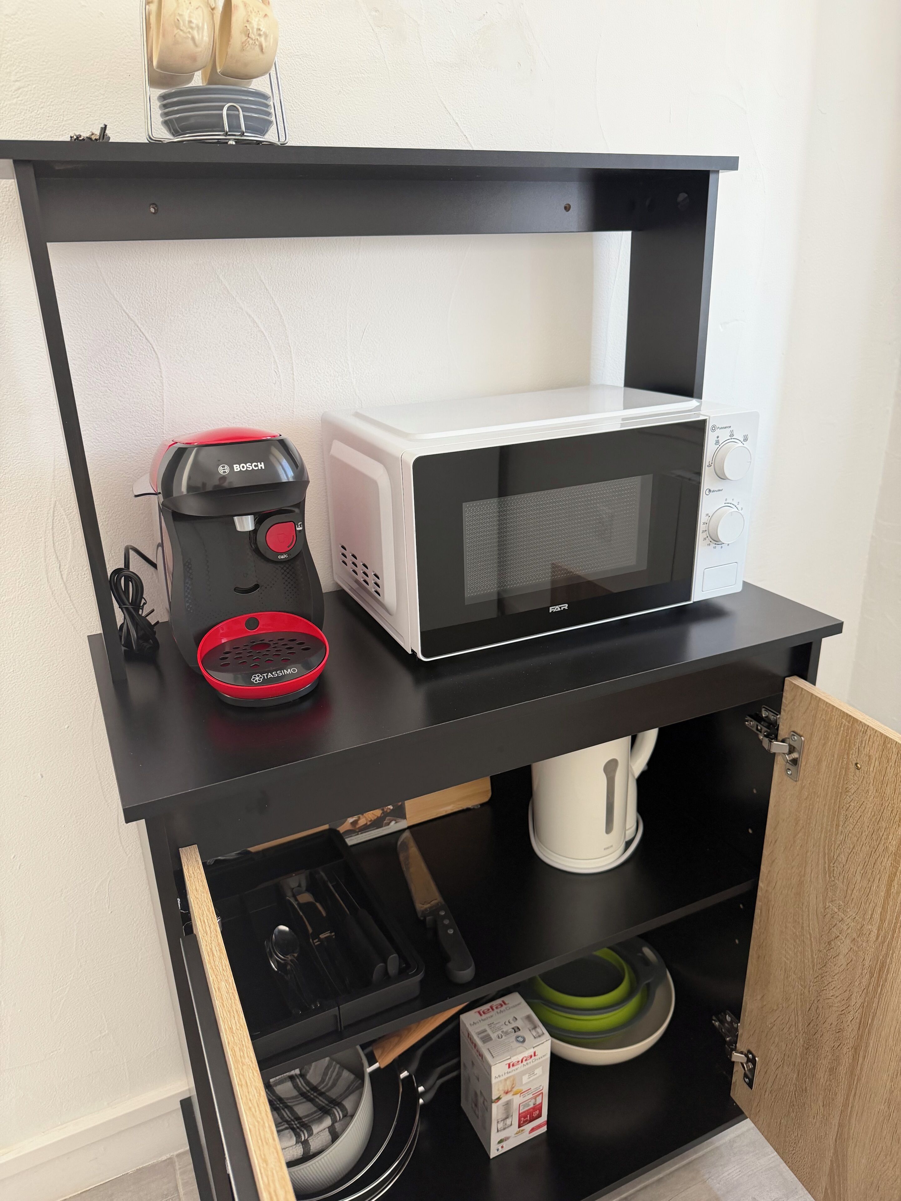 Una cocina con microondas, tostadora y cafetera sobre un estante negro, con un armario debajo.