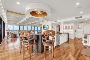 A spacious kitchen with a central island, wooden chairs, and a large window overlooking the ocean. - Mansions By The Sea 1201a - Premier (Treasure Island)