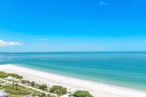 Ein Strand mit klarem, blauem Wasser, einem sandigen Ufer und etwas Grün im Vordergrund.