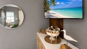 A modern room with a TV displaying a beach scene, a round mirror, a decorative bowl with seashells, and a wooden cabinet. - Charm, comfort and an exceptional location ,  Free parking (Miramar)