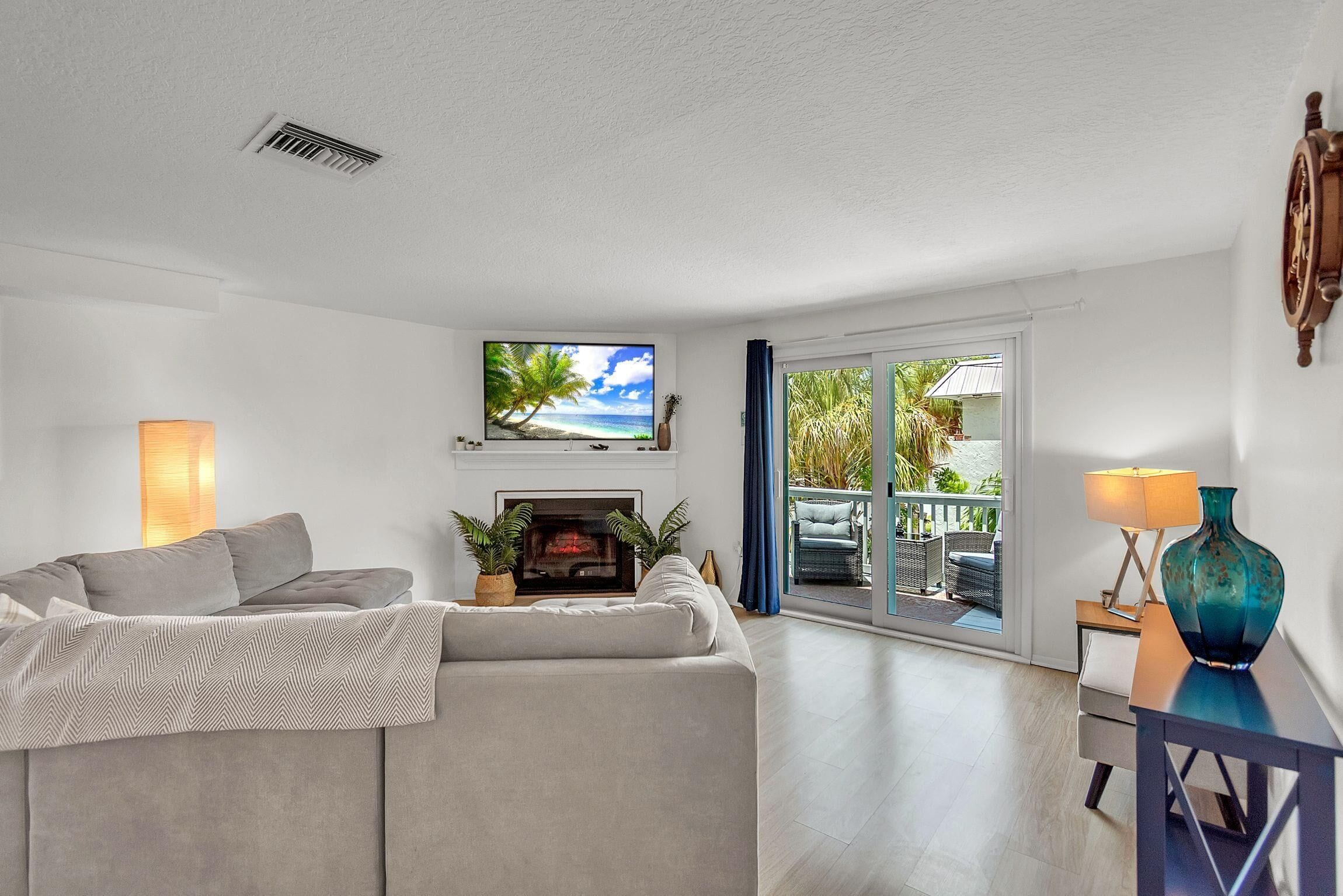 A modern living room with a sofa, a flat-screen TV, a fireplace, and a view of the outdoors.