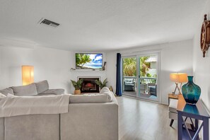 A modern living room with a sofa, a flat-screen TV, a fireplace, and a view of the outdoors. - Beach Blast Retreat (Indian Rocks Beach)