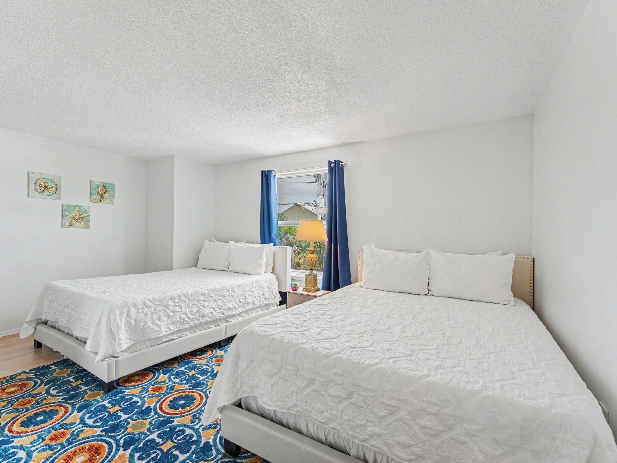 A hotel room with two beds, a patterned rug, and artwork on the wall.