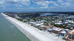 Ovenudblik over en kystby med strand, bygninger og en lysthavn.