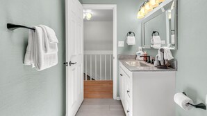 Et badeværelse med hvid kommode, spejl, bøjle til håndklæder og toiletpapirholder.