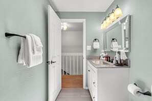 A bathroom with a white vanity, a mirror, a towel rack, and a toilet paper holder. - Beach Blast Retreat (Indian Rocks Beach)