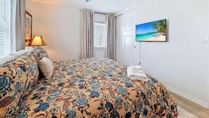 Ein Schlafzimmer mit einem Bett, einem Deckenventilator, einem Fernseher und einem Fenster mit Vorhängen.