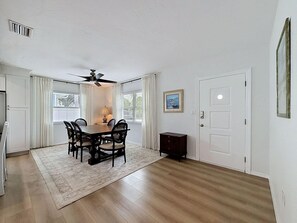A dining room with a table, chairs, a ceiling fan, and a rug. - The Blue Heron (St. Pete Beach)