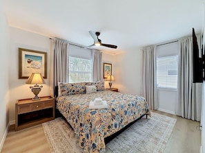 A bedroom with a bed, two bedside tables, a ceiling fan, and a window with curtains. - The Blue Heron (St. Pete Beach)