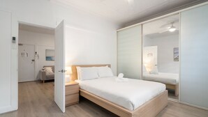 Hotellihuone, jossa on sänky, yöpöytä ja suuri peili.
