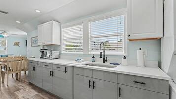 A modern kitchen with a large island, white cabinetry, and a view of the outdoors through the windows.