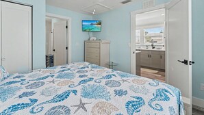 A bedroom with a bed, a ceiling fan, a TV, a dresser, and a bathroom visible through an open door. - Sunset Paradise (Madeira Beach)