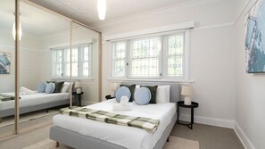 Ein Schlafzimmer mit einem großen Spiegel, einem Bett mit kariertem Überwurf, zwei Nachttischen mit Lampen und einem Fenster mit Buntglas.