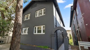 Um edifício de dois andares com fachada escura, janelas emolduradas de branco e entrada de tijolos.