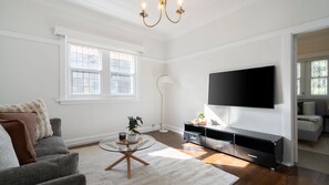 Ein Wohnzimmer mit einer Couch, einem Glastisch, einem Fernseher und einer Stehlampe.
