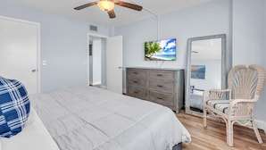 Ein Schlafzimmer mit einem Bett, einem Deckenventilator, einer Kommode, einem Sessel und einem an der Wand befestigten Fernseher.